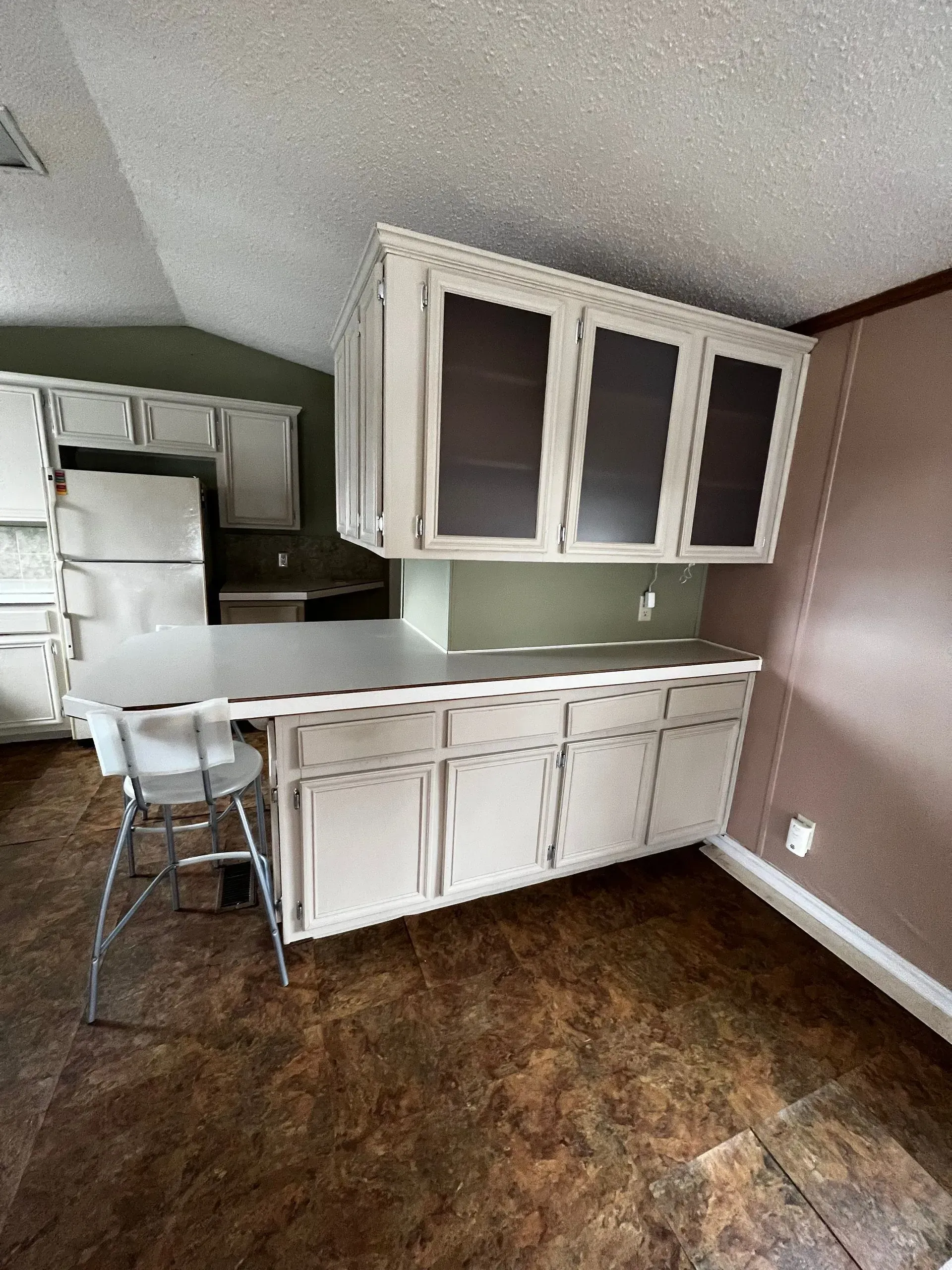 Kitchen with white cabinets, light countertop, and bar stool. Brown floor.
