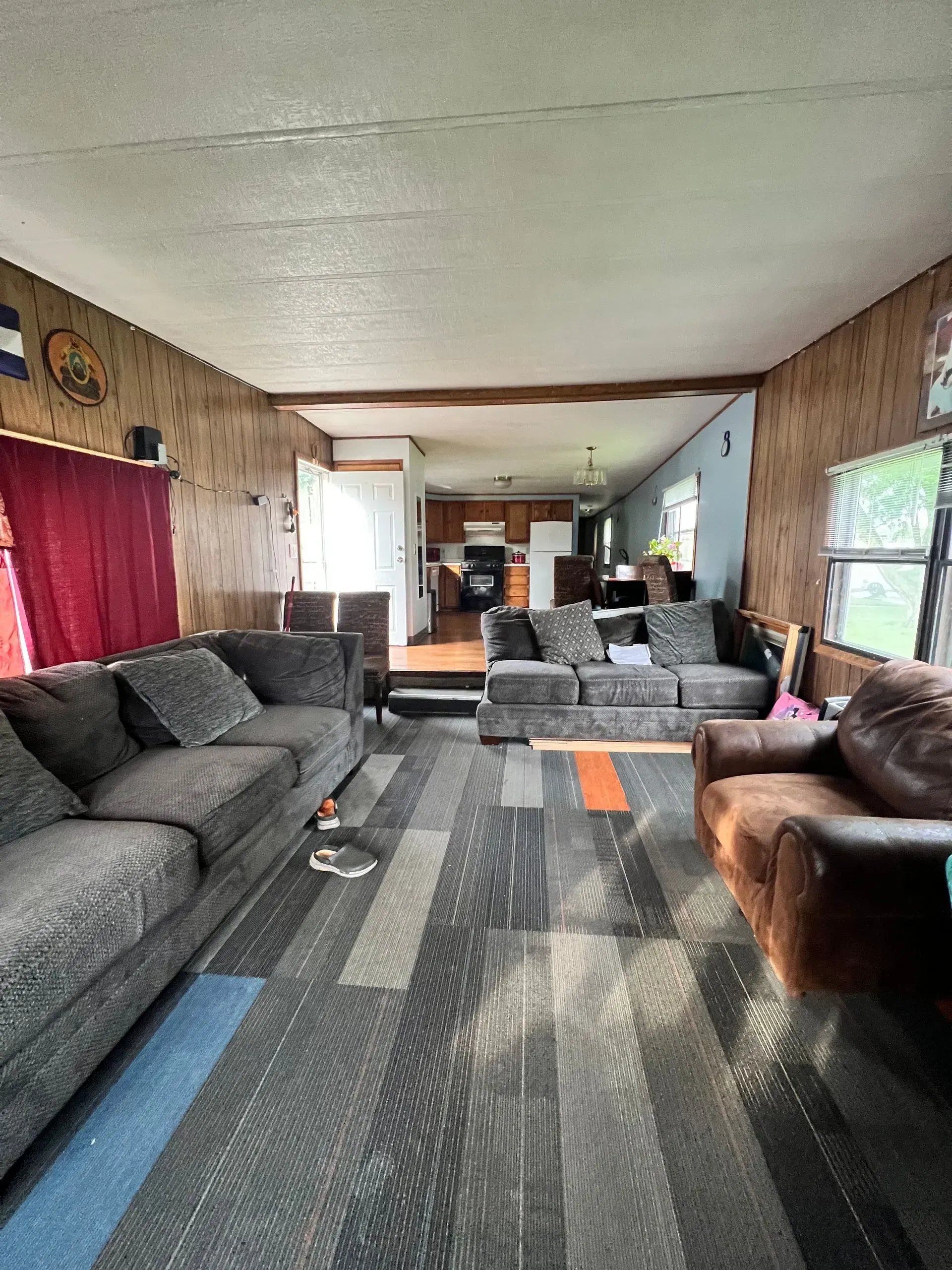 Living room with two gray sofas and one brown chair, wood panel walls, and patterned carpet.