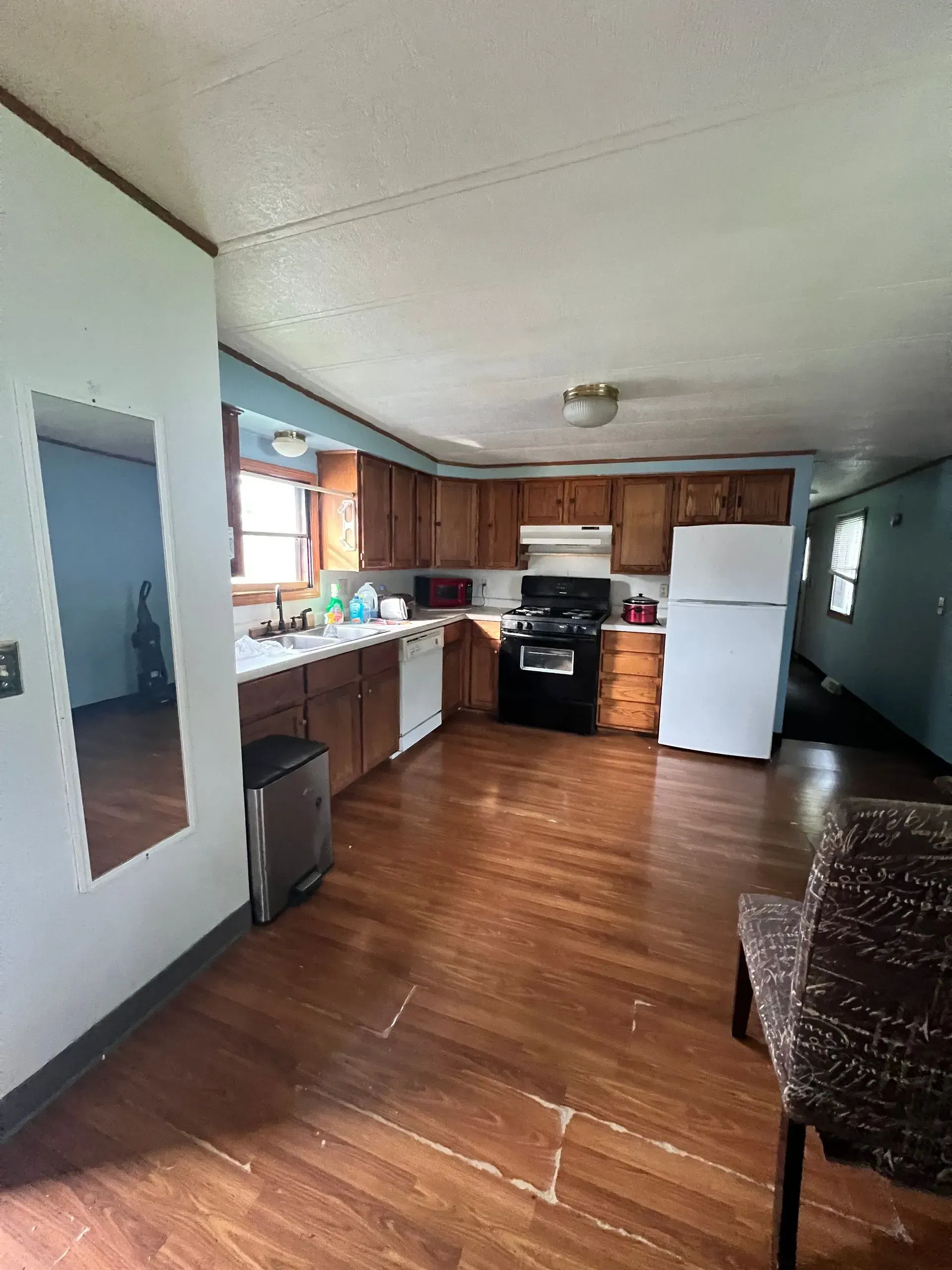 Kitchen with wooden cabinets, appliances, and brown flooring. A mirror reflects a blue wall.