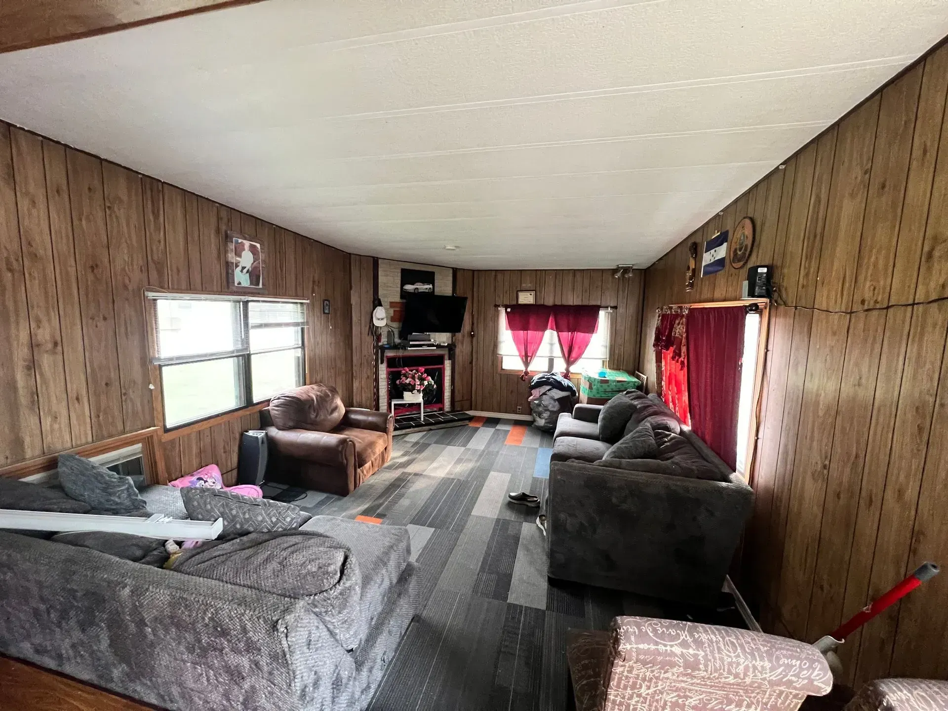 Living room with wood paneling, multiple couches, window, and TV.
