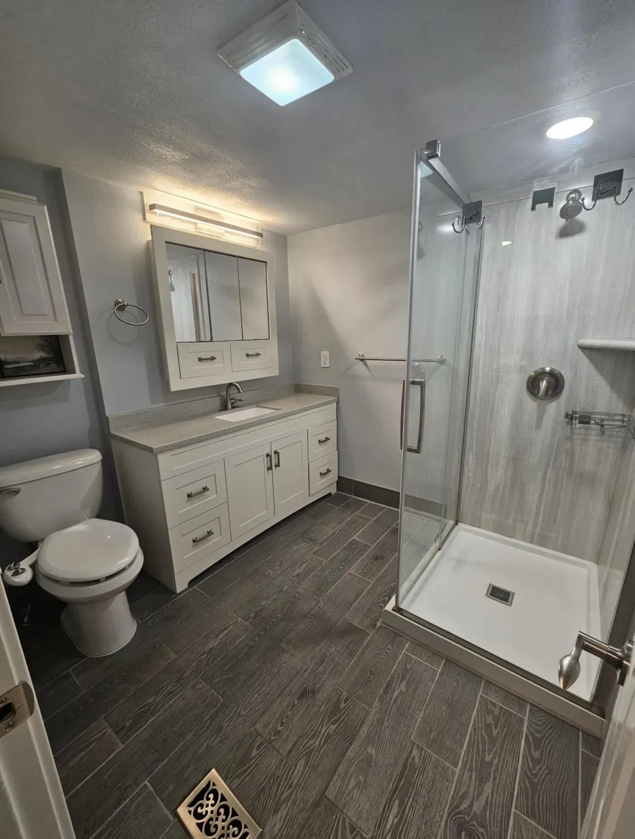 Modern bathroom with gray tiled floor, white vanity, and glass shower.