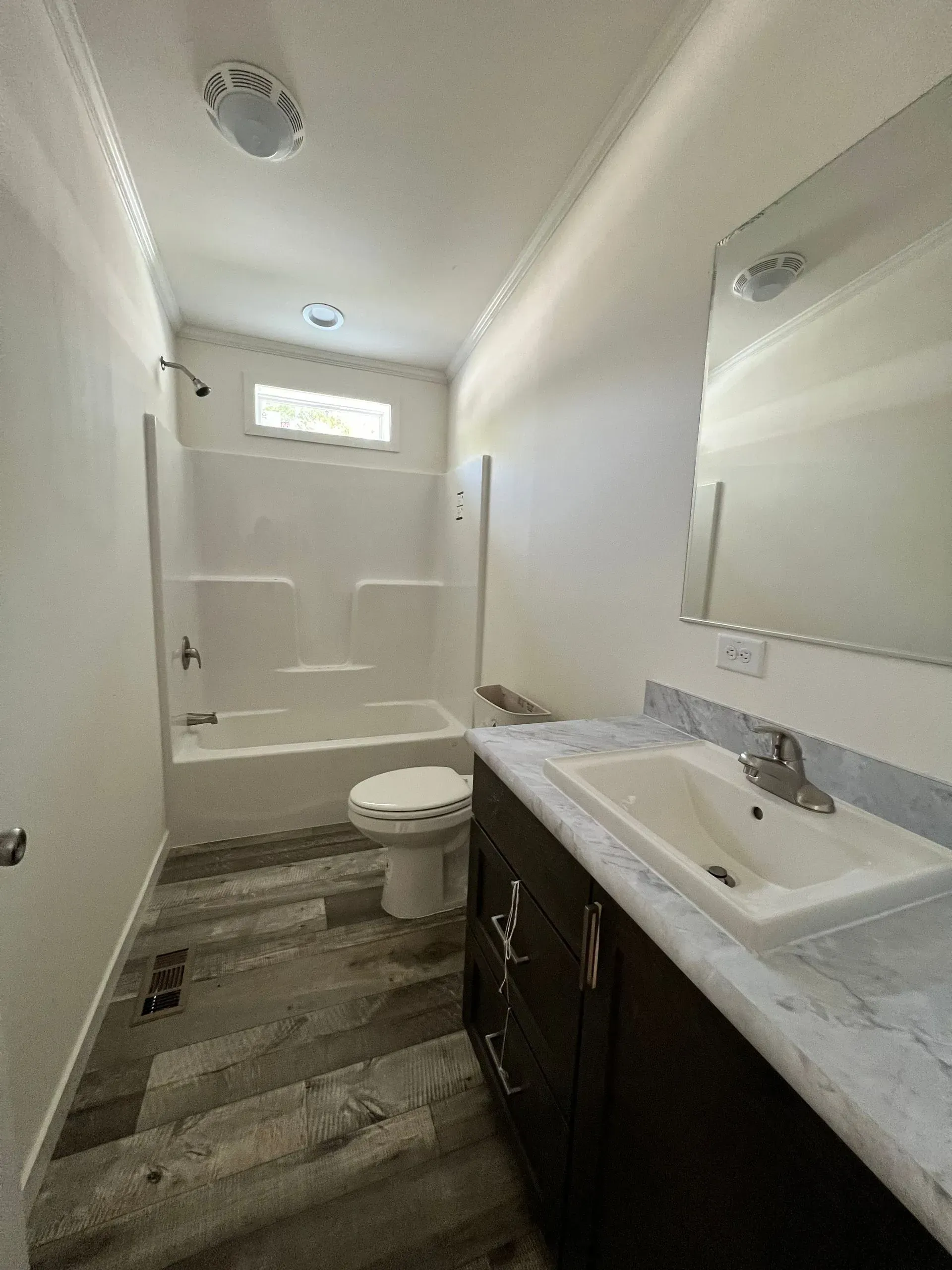 Bathroom with white walls, shower/tub, toilet, dark vanity, and wood-look floor.