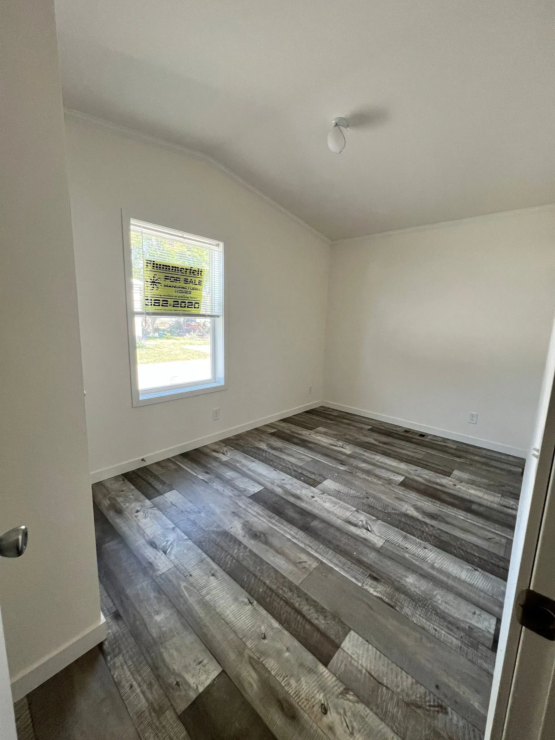 Empty room with wood-look flooring, white walls, and a window.