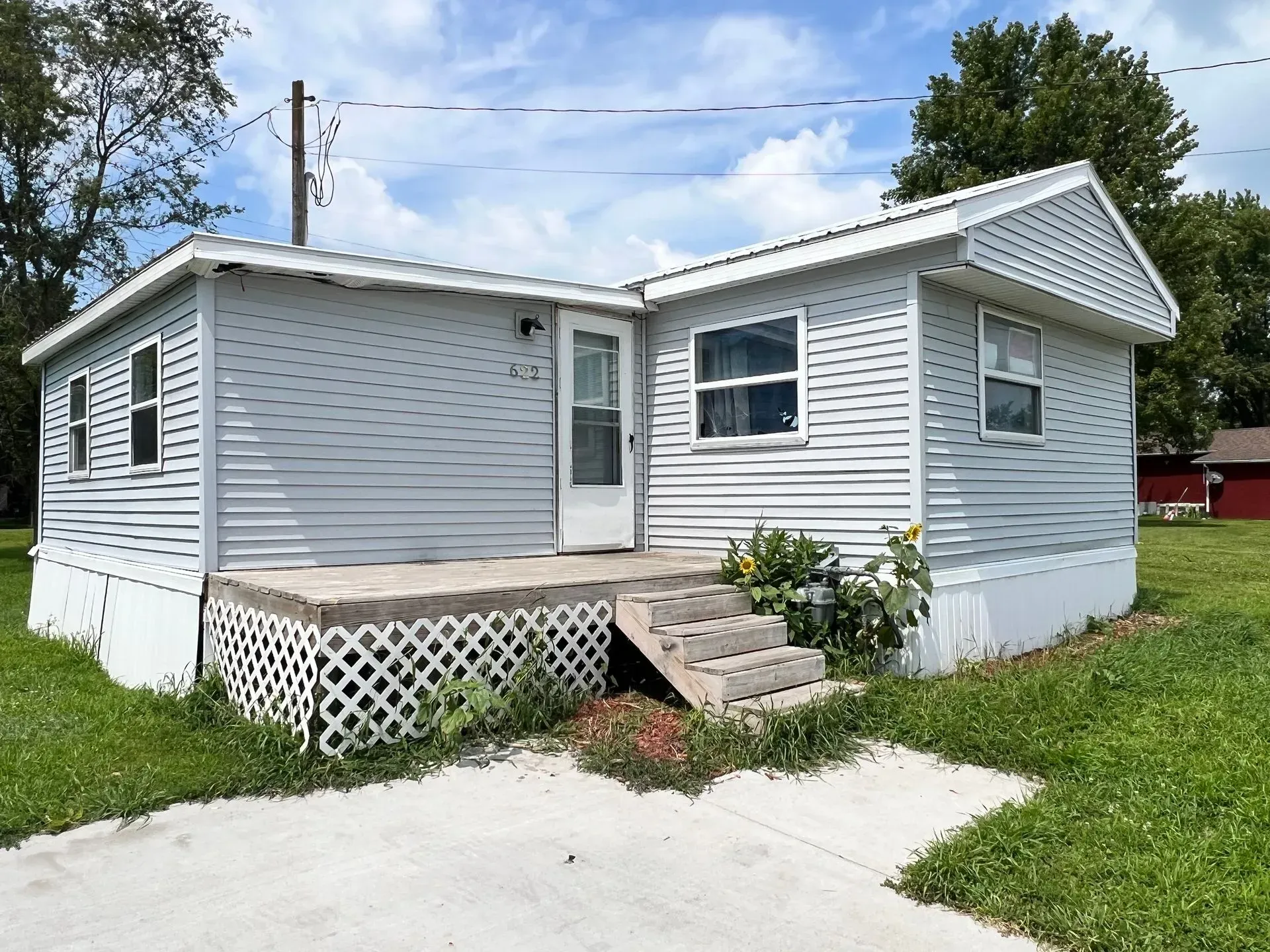 A single-story, light gray house with a small porch and steps. Blue sky, green grass.