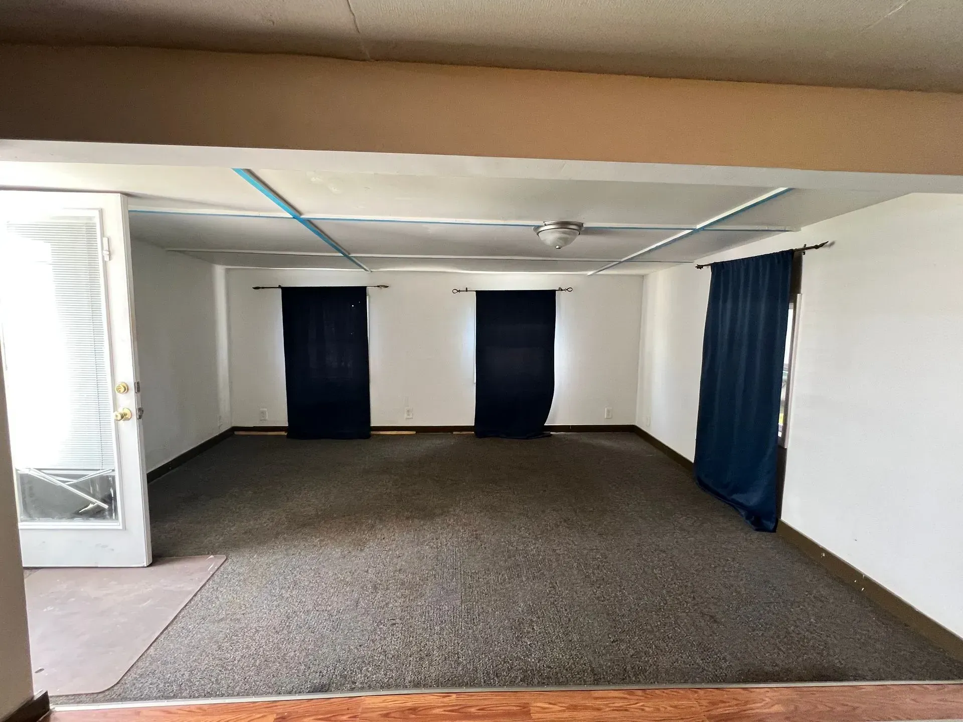 Empty room with blue curtains, tan ceiling, and brown carpet. A door is on the left.