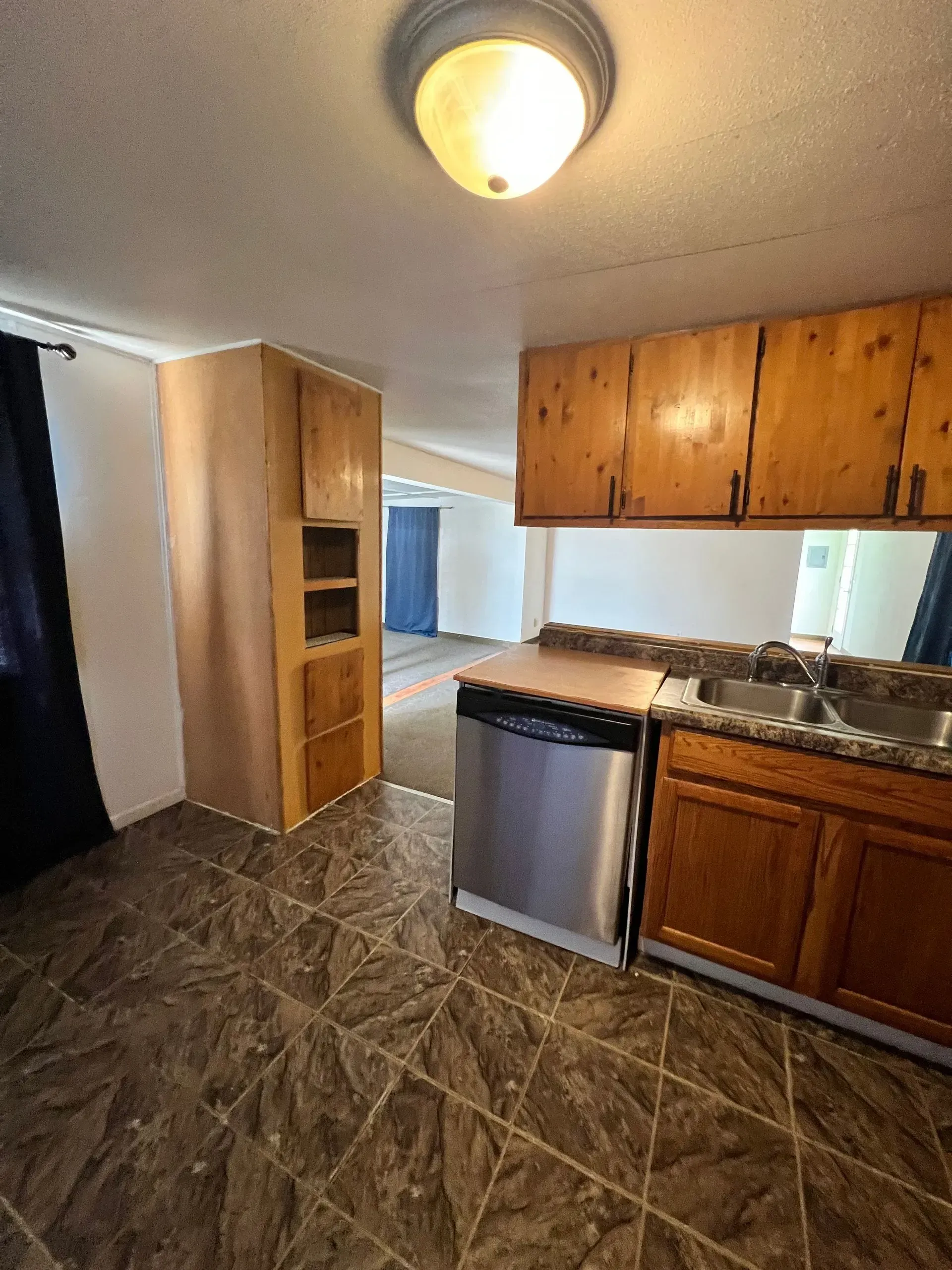 Kitchen with wood cabinets, stainless steel dishwasher, and brown tile floor.