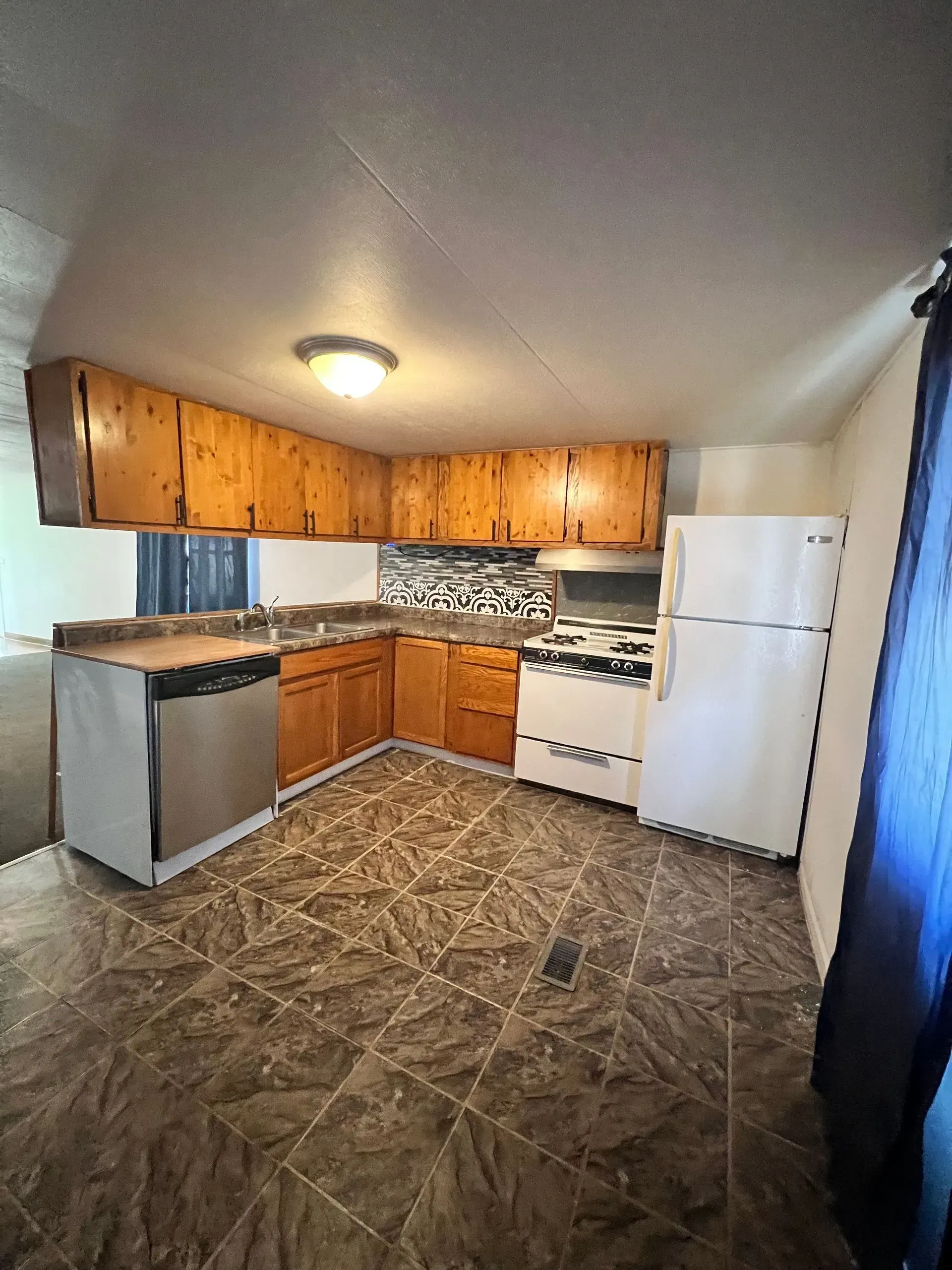 Kitchen with wooden cabinets, stainless steel dishwasher, white refrigerator, and brown patterned floor.