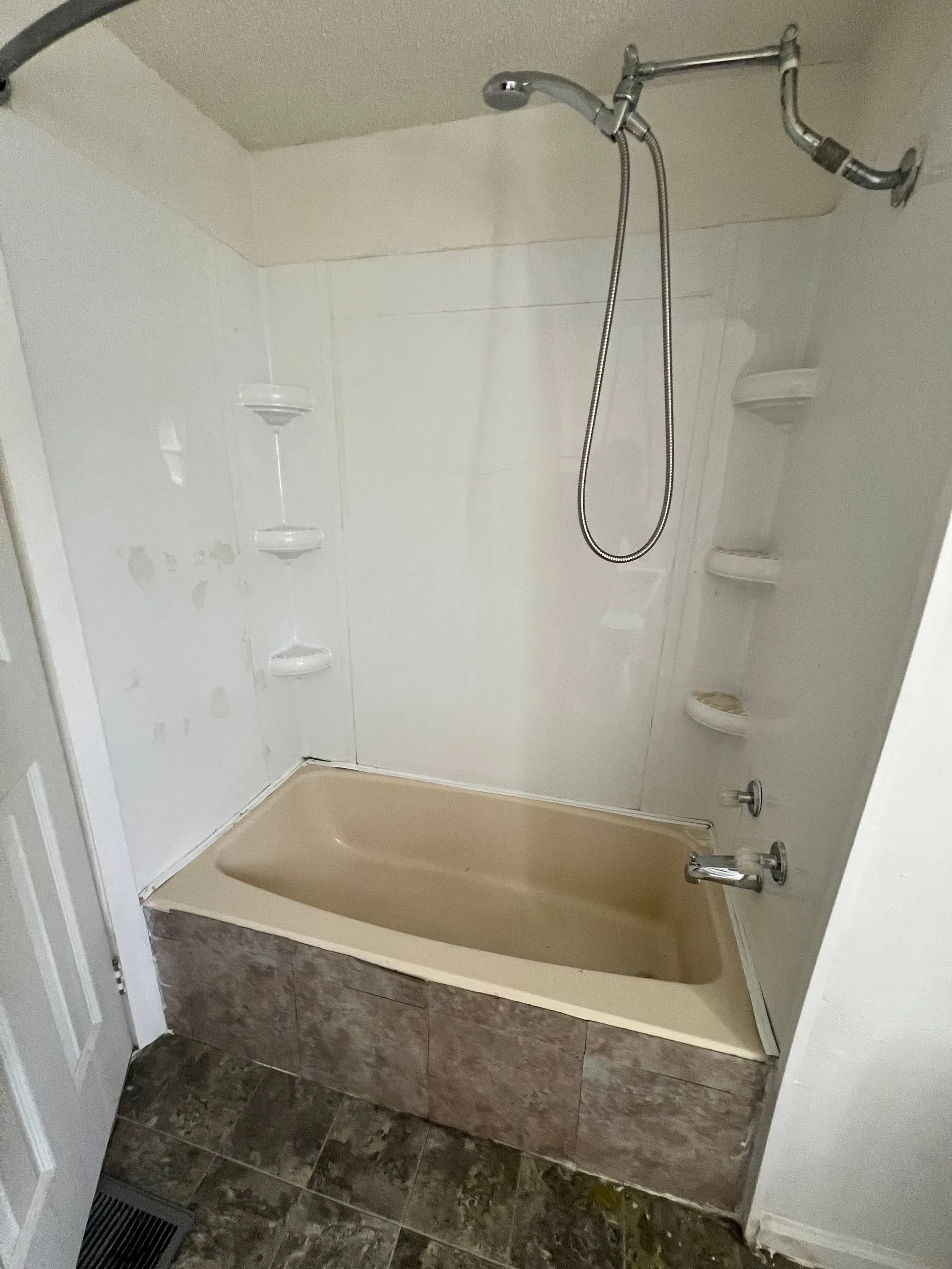Shower and bathtub combo with white surround, tan tub, and showerhead.