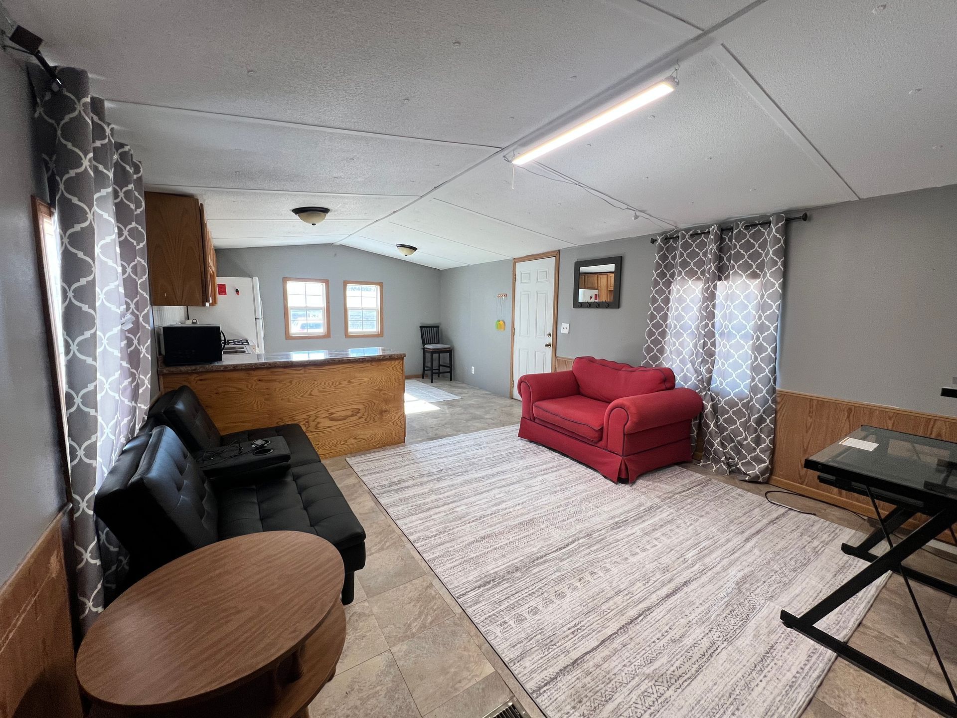 Living room: gray walls, red sofa, black futon, brown bar, kitchen, rug, and windows.  