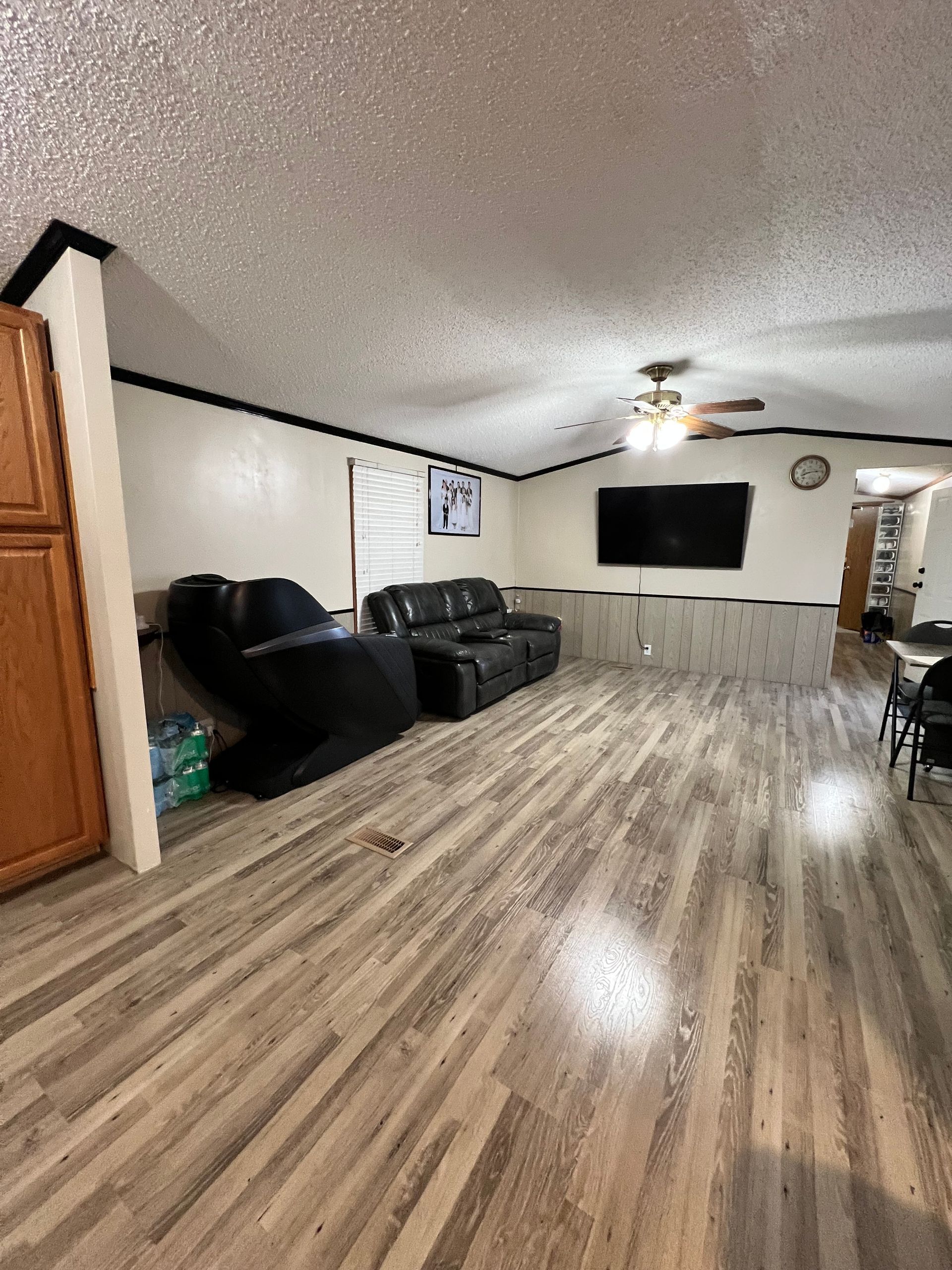 Living room with black leather furniture, wood-look flooring, and a mounted TV.