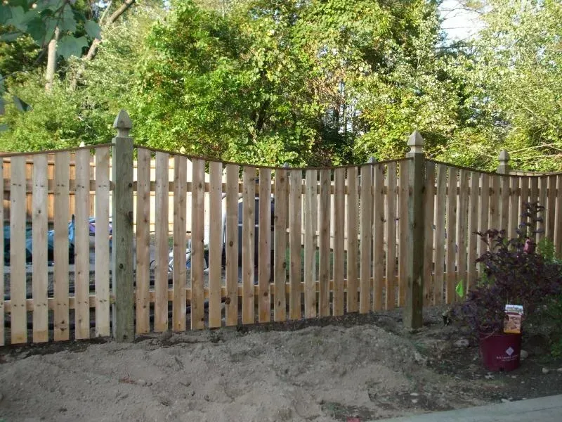 A wooden picket fence is surrounded by trees and dirt