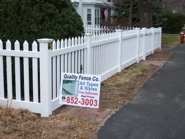 A white picket fence with a sign that says quality fence co.