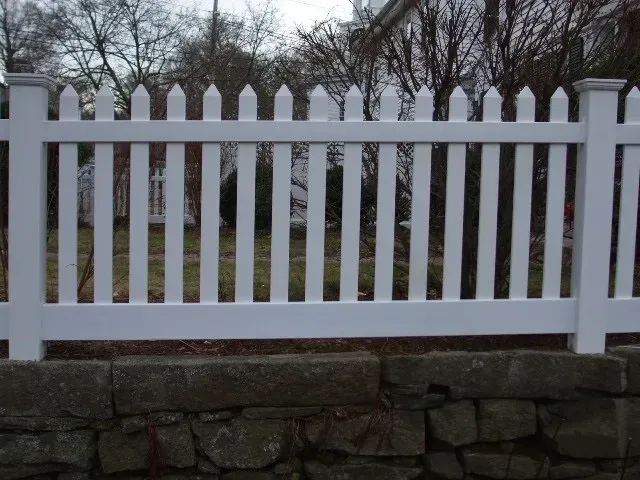 A white picket fence is next to a stone wall