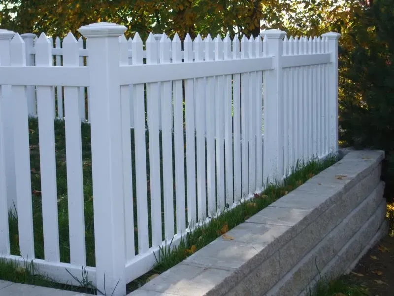 A white picket fence surrounds a stone wall