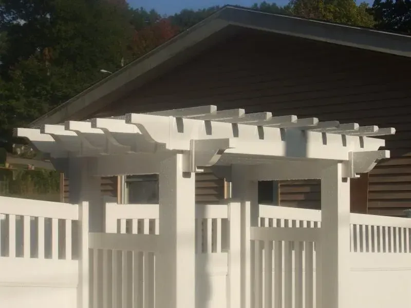 A white pergola with a fence in front of a house