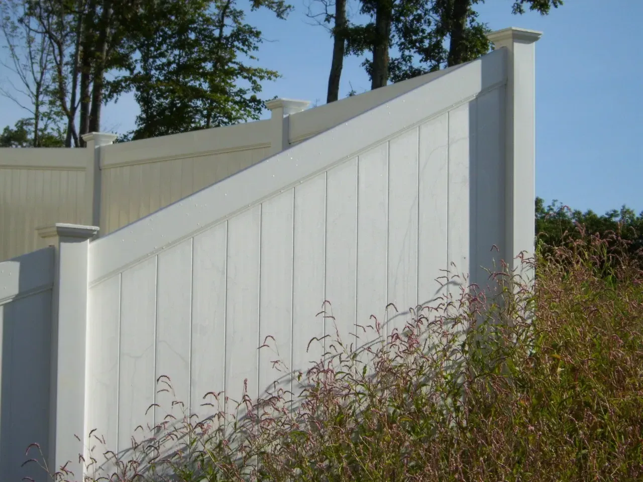 A white fence is surrounded by tall grass and trees