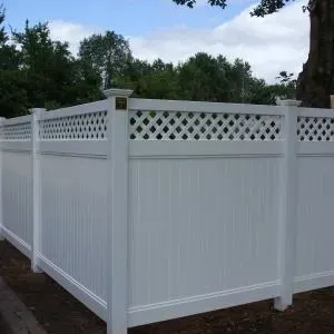 A white vinyl fence with a lattice design and a tree in the background.