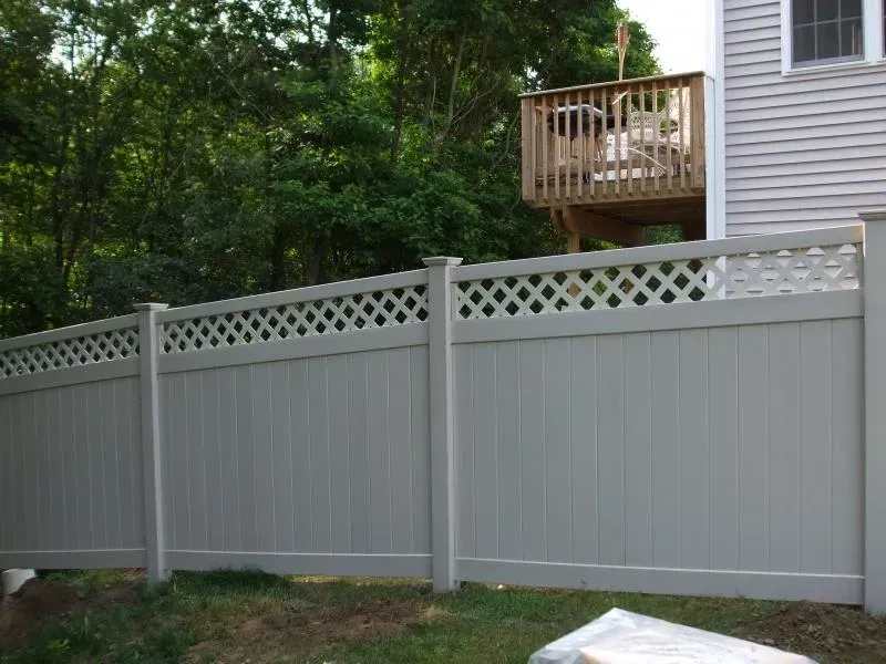 A white fence with a lattice design is in front of a house with a deck.