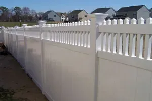 A white vinyl fence with a row of houses in the background.
