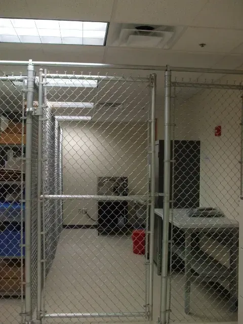 A room with a chain link fence and a red trash can