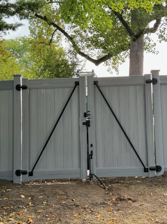 Gray vinyl gate with black diagonal supports and a tripod-mounted device in front.