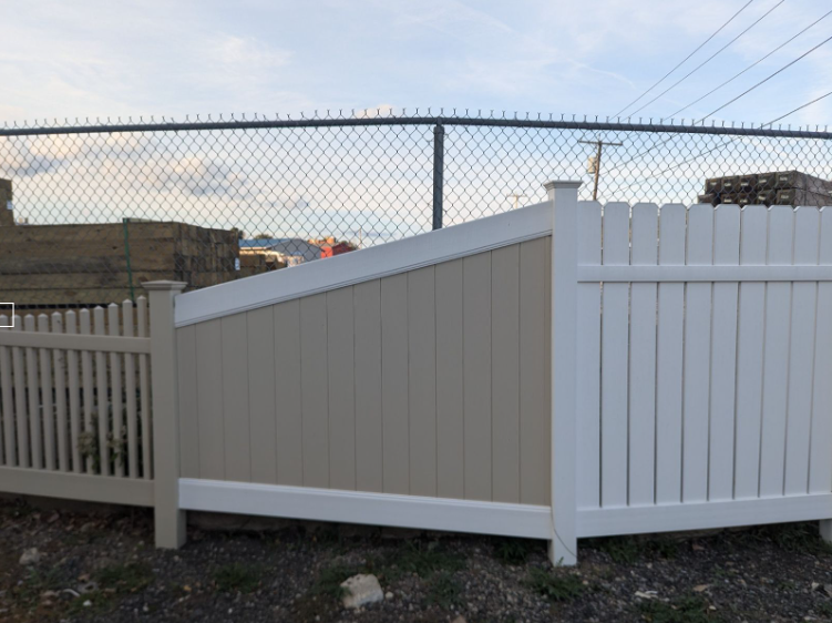 Tan and white vinyl fence, angled section, with a chain-link fence in the background.