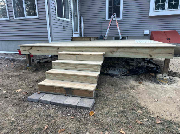 A new wooden deck with stairs leading down to a brick pathway in a yard.