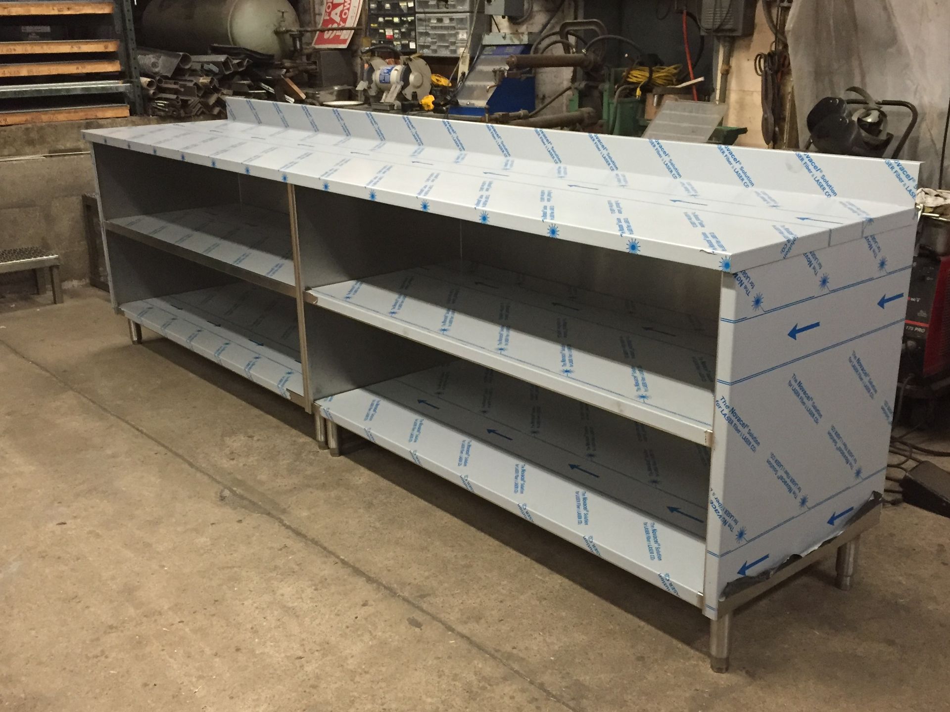 A stainless steel cabinet with shelves is sitting on the floor in a workshop.