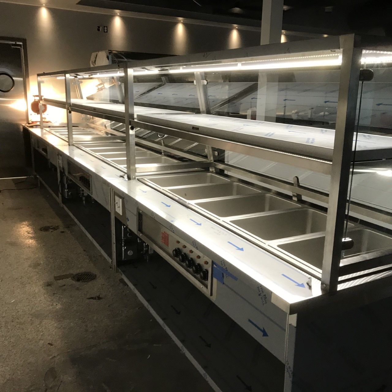A long stainless steel counter with lots of sinks under a glass display case