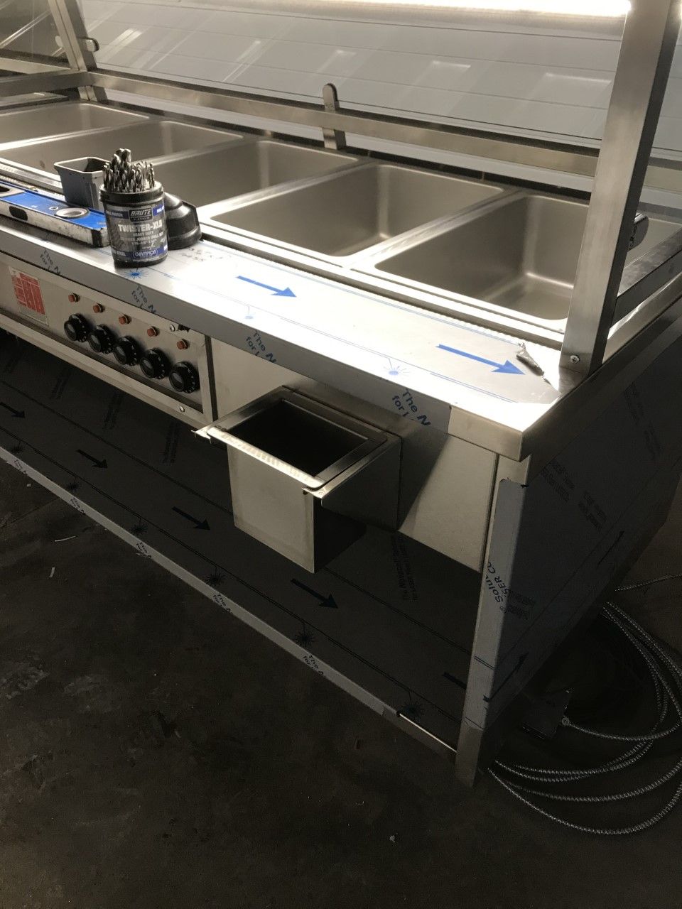 A stainless steel counter with three sinks and a drawer underneath it.