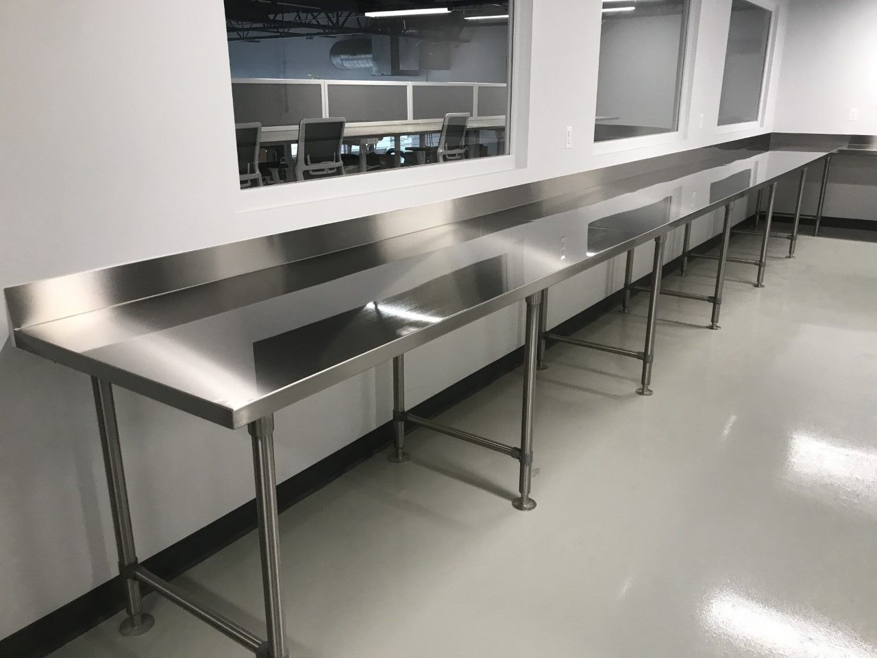 A row of stainless steel tables in a room with a window.
