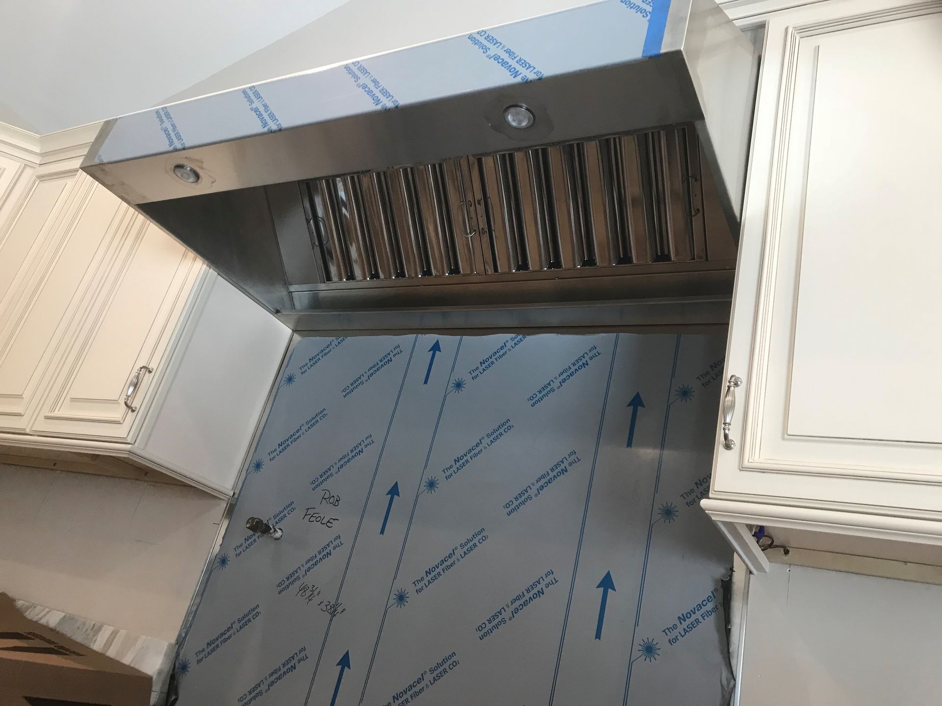 A kitchen with white cabinets and a stainless steel hood