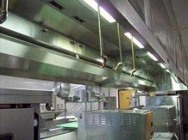 A kitchen with stainless steel appliances and a hood hanging from the ceiling.