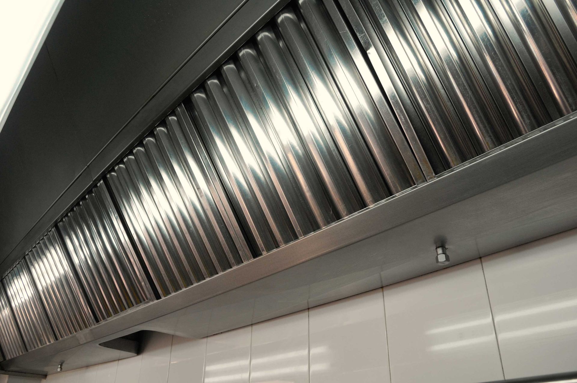 A stainless steel hood is hanging from the ceiling in a kitchen.