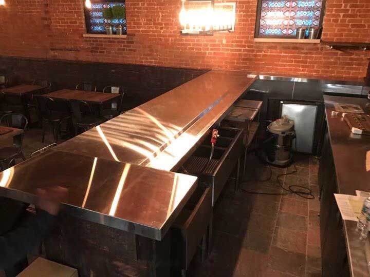 A stainless steel bar in a restaurant with tables and chairs.