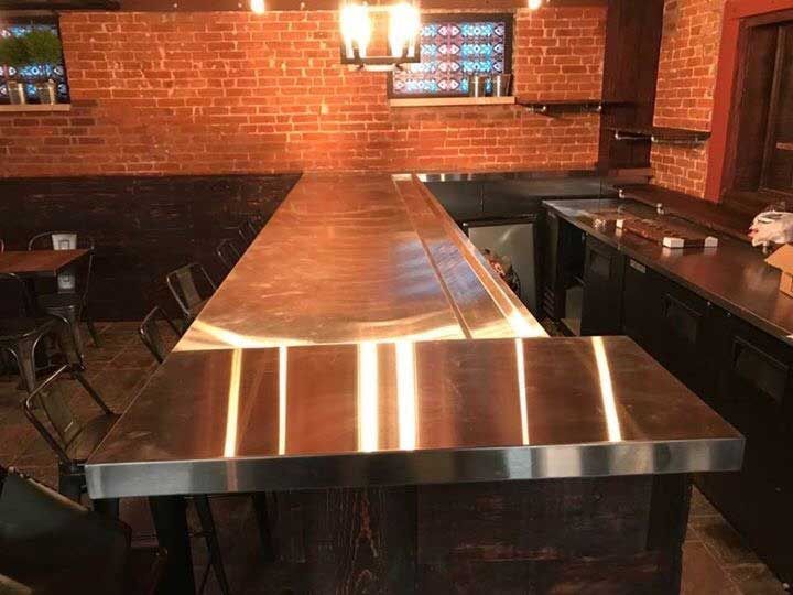 A long stainless steel bar in a restaurant with tables and chairs.