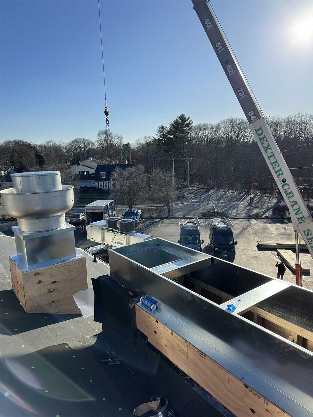 A crane is lifting a metal pipe on top of a roof.