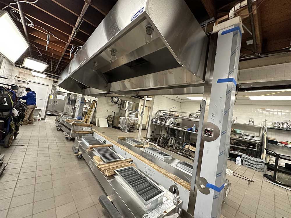 A kitchen with a lot of stainless steel appliances and a motorcycle parked in the background.