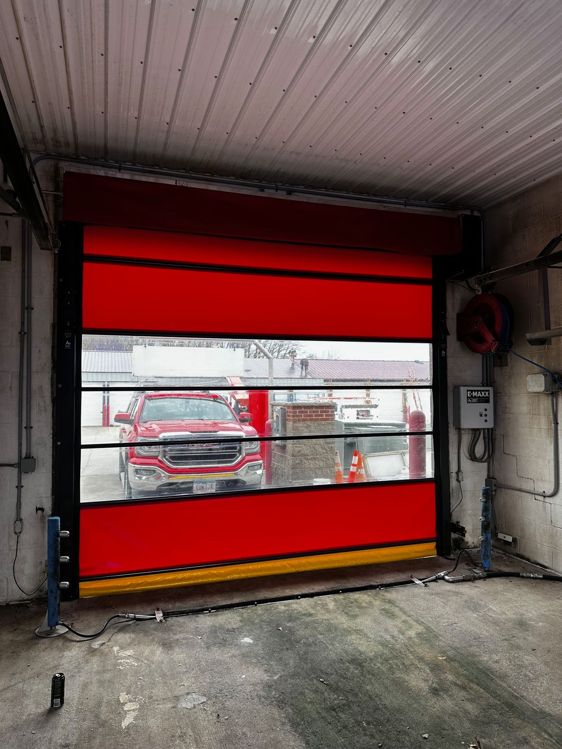 Red, high-speed roll-up door partly open, revealing a red pickup truck inside. Black frame, yellow base, in a garage.