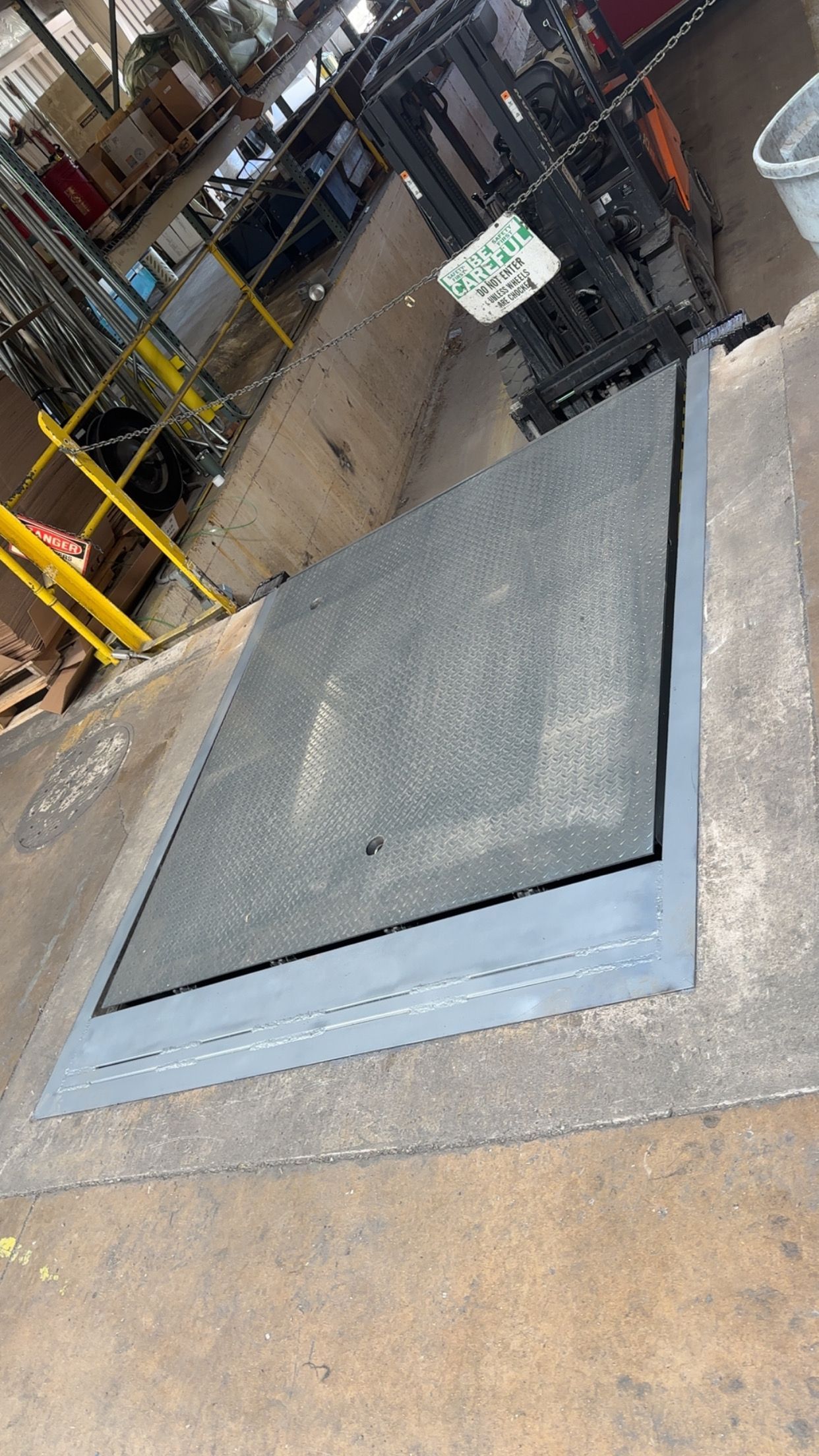 Warehouse floor hatch with a large gray metal cover and concrete surroundings