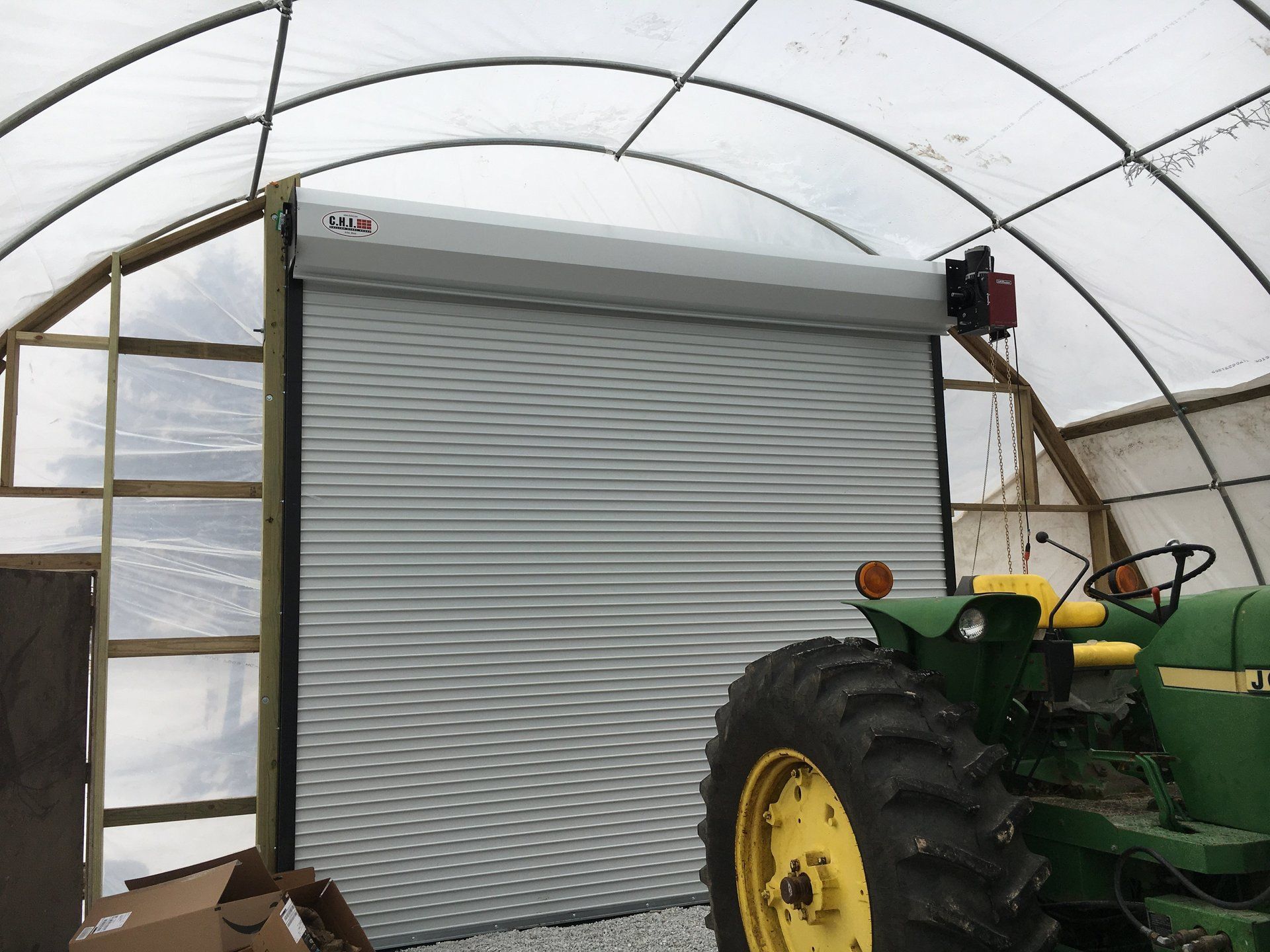 A green tractor is parked in front of a greenhouse.