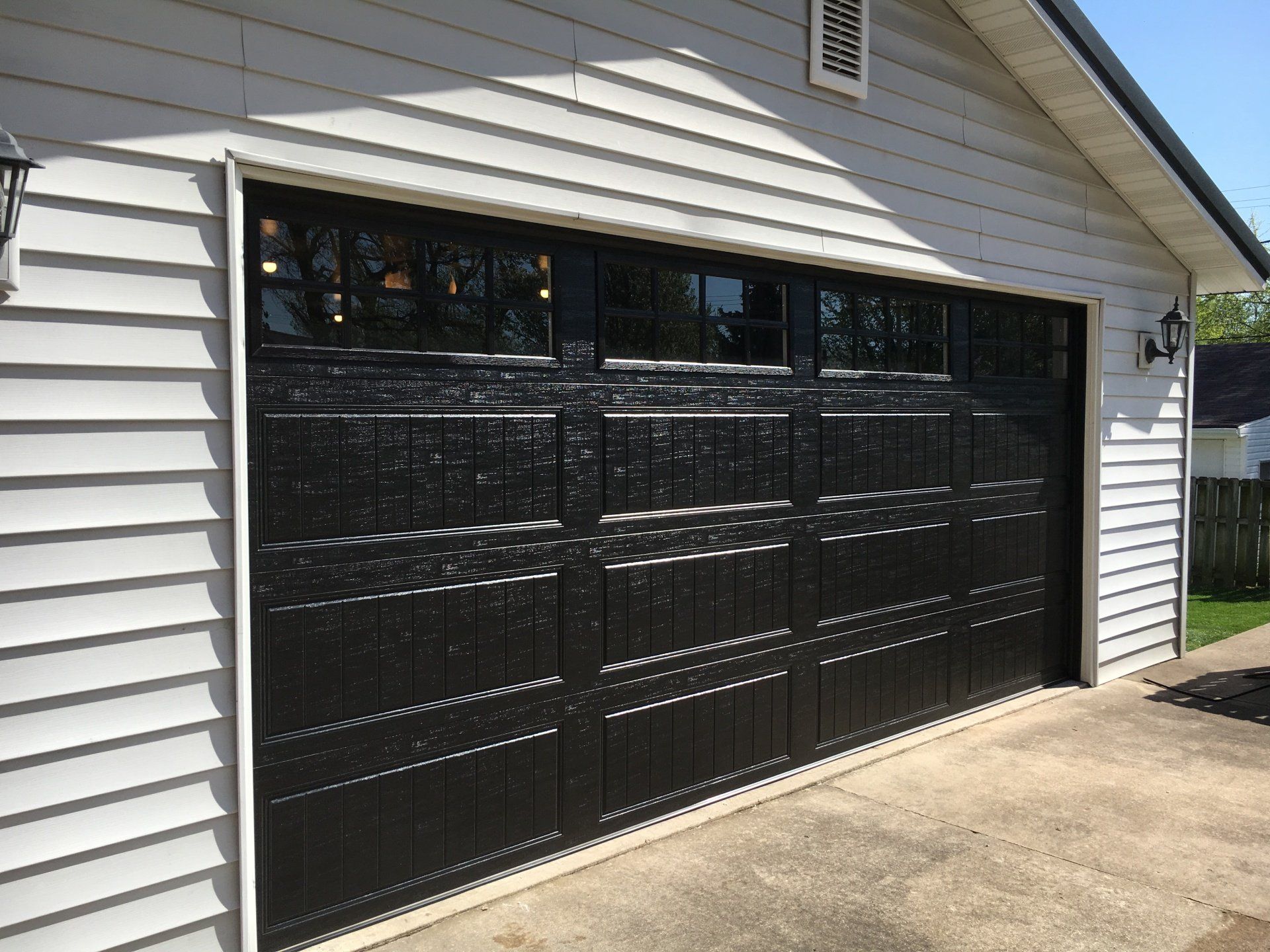 A black garage door is on a white house.