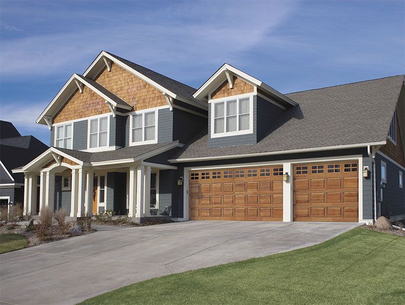 Two-story house with blue siding, brown wooden garage doors, and a concrete driveway