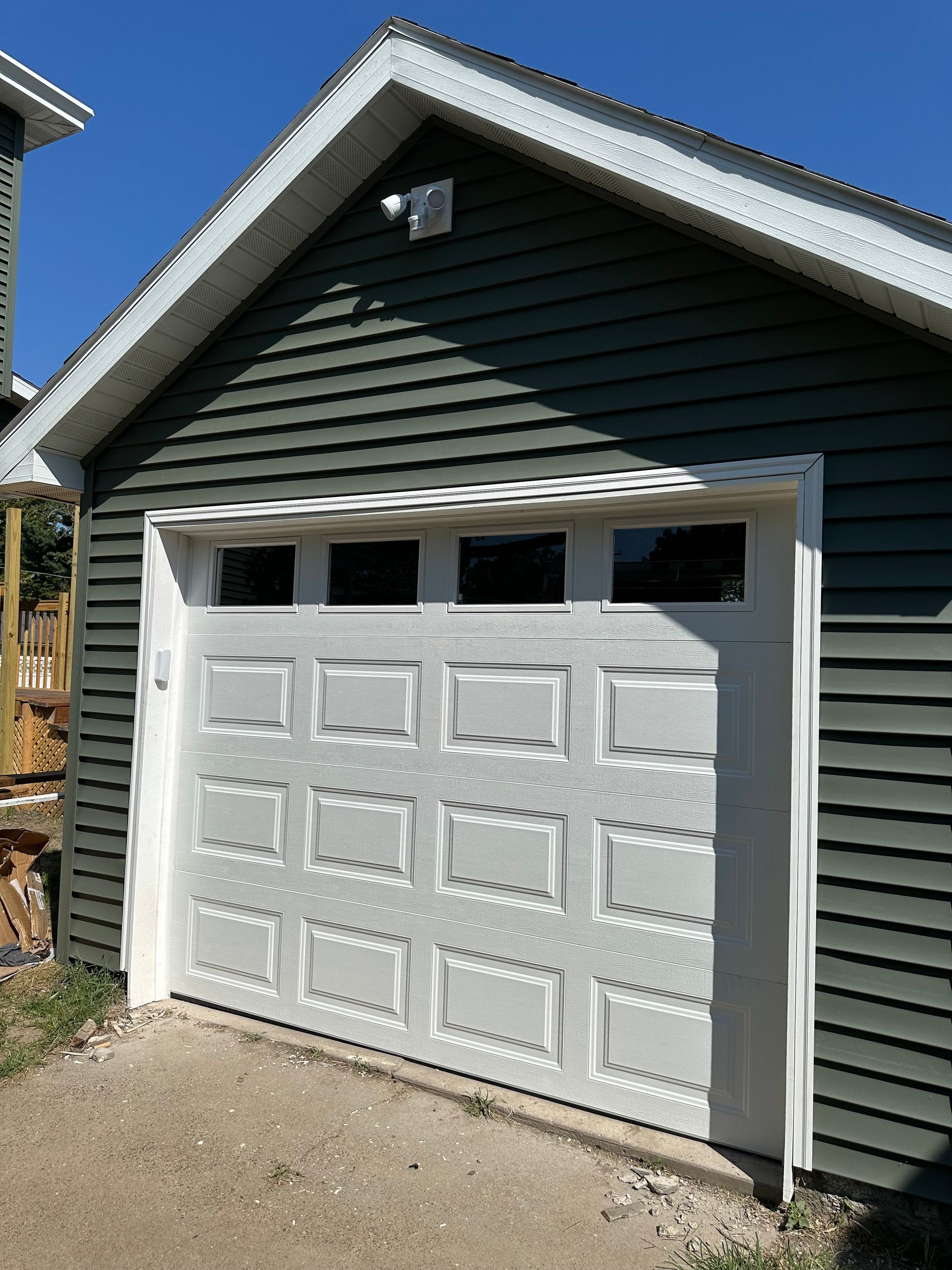 A white garage door is sitting in front of a green house.