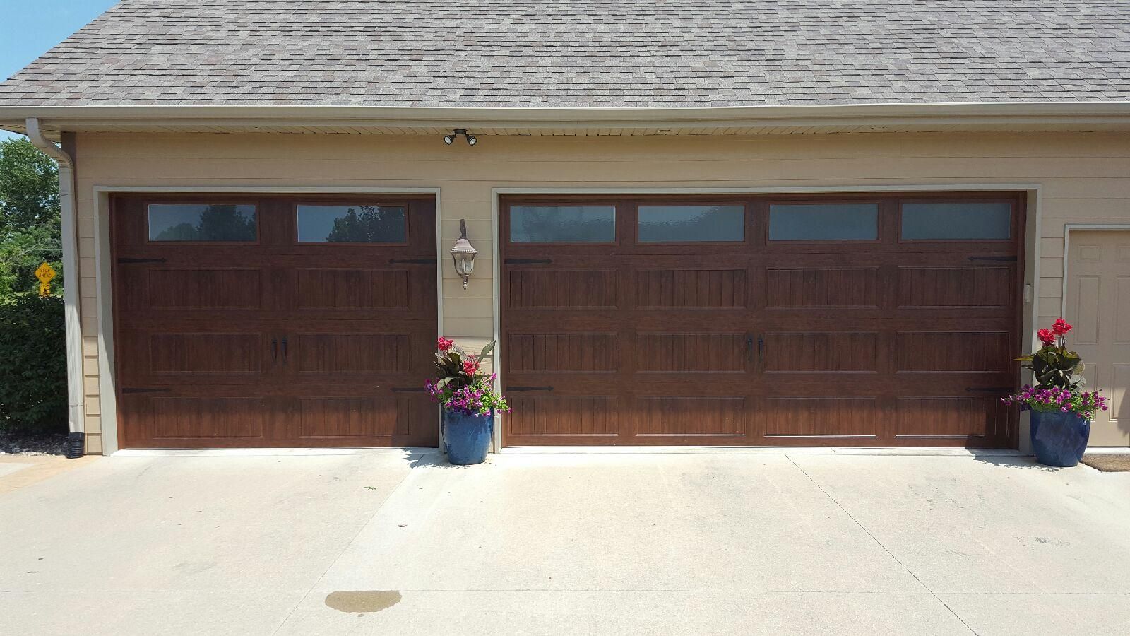 A garage with two garage doors and two potted plants in front of it.