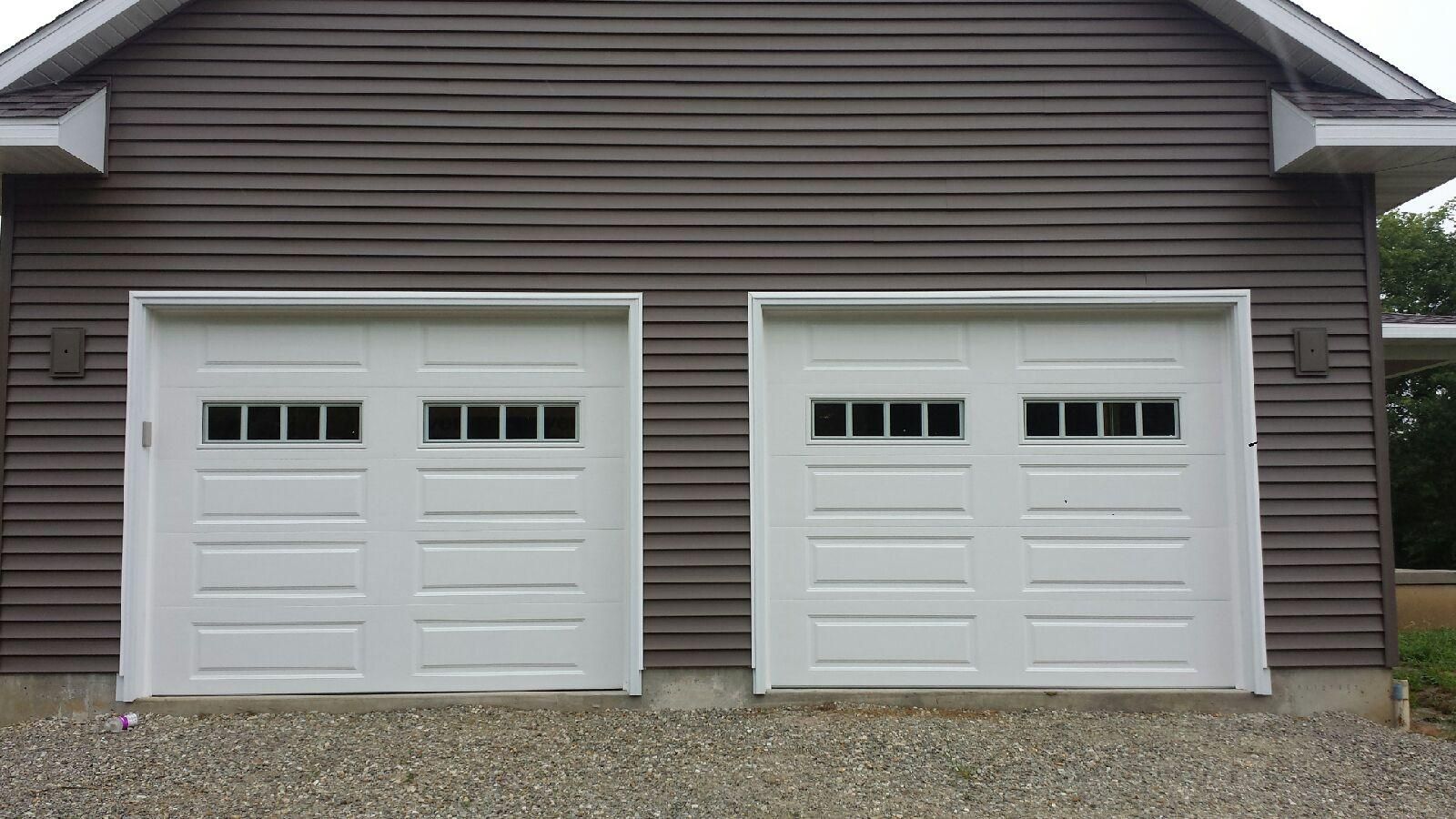 A garage with two white garage doors and a brown siding