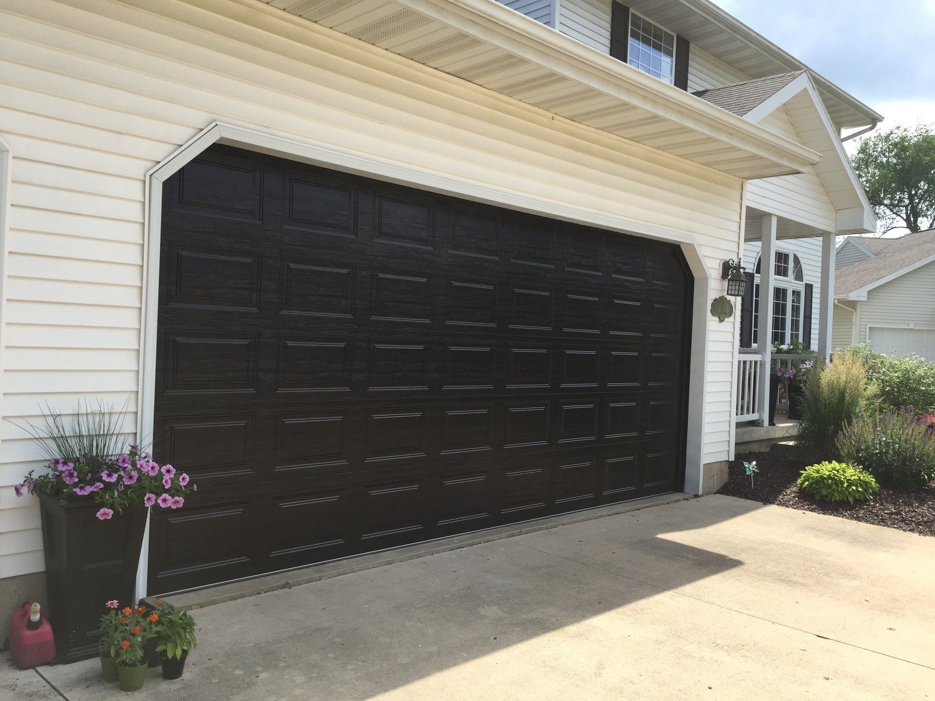 A black garage door is sitting in front of a white house.