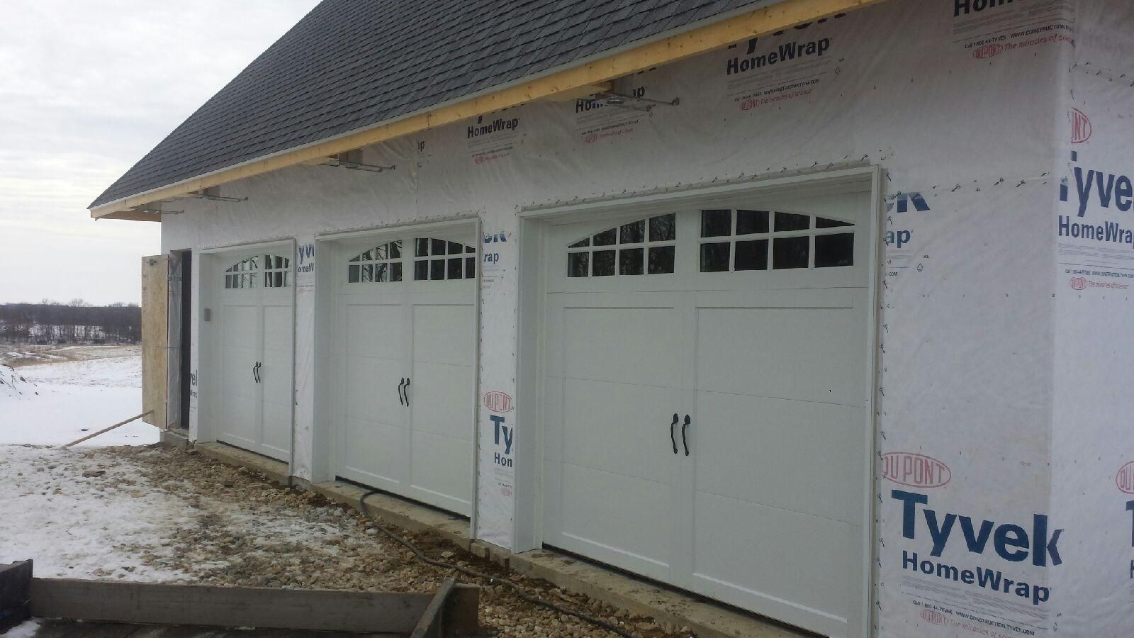 A row of white garage doors on a house under construction.
