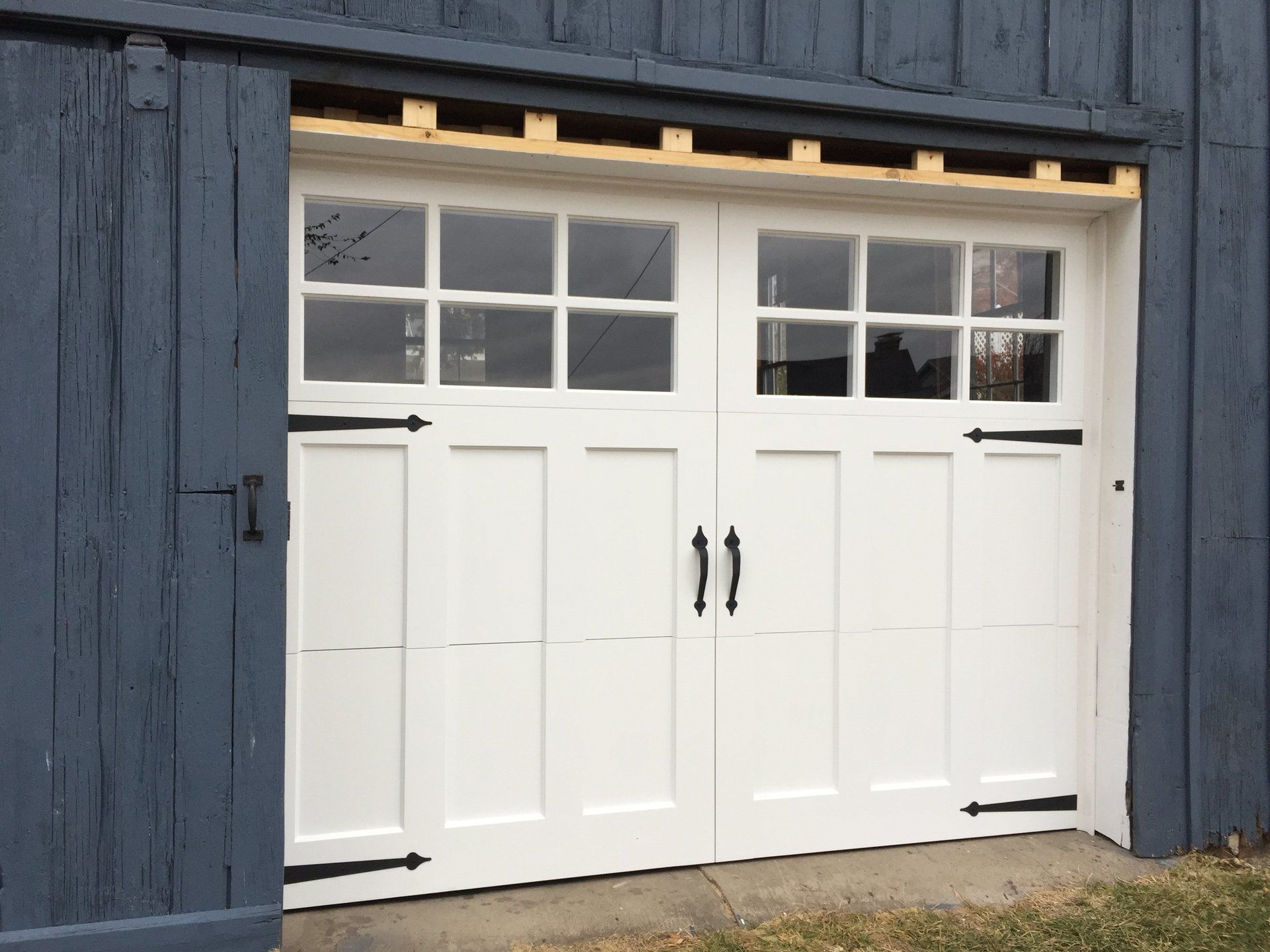 A white garage door with black handles is on a blue building.