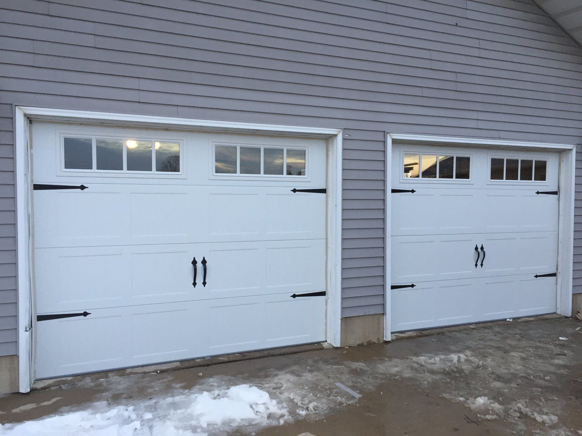 Two white garage doors with black handles are sitting next to each other on the side of a building.